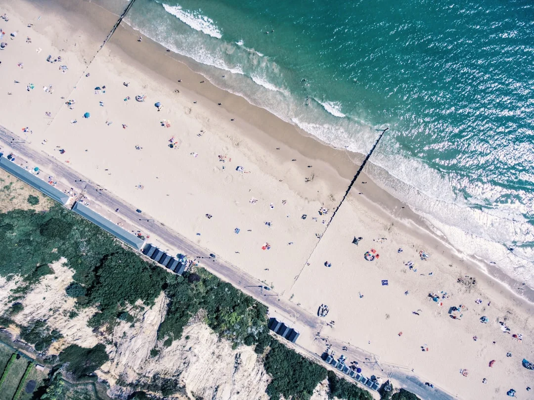 Aerial view of a sandy beach in Bournemouth with people sunbathing next to turquoise ocean waves