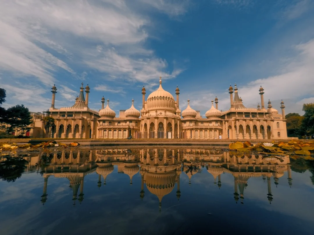 The Royal Pavilion in Brighton with its ornate domes and minarets reflected in a calm pond under a blue sky