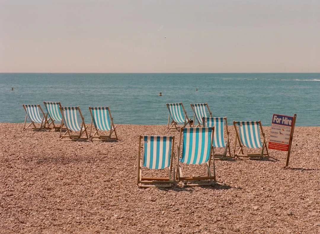 Blue and white striped deck chairs on a pebble beach facing the sea under a clear sky