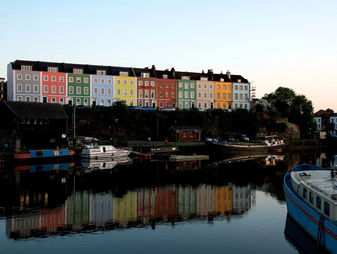 Row of colorful houses overlooking Bristol Harbourside at sunset, with reflections on the calm water and boats
