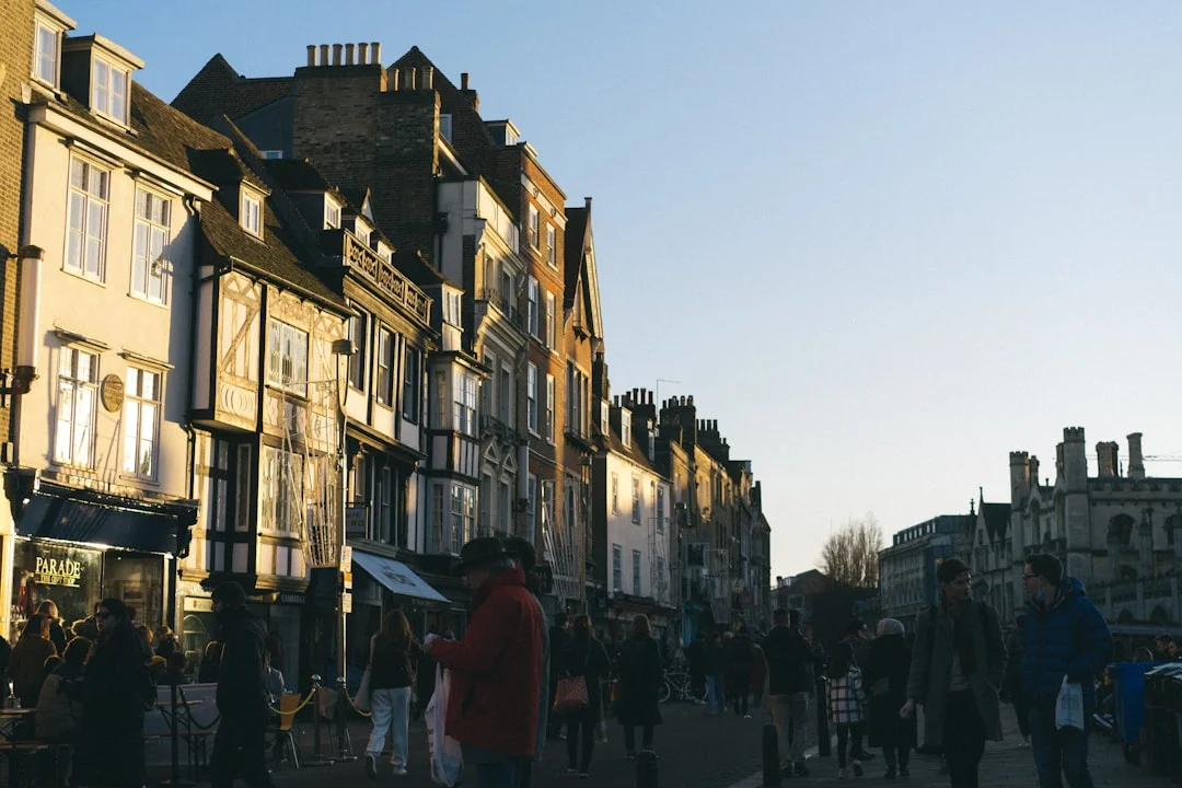People walking along a historic Cambridge street lined with old buildings during golden hour