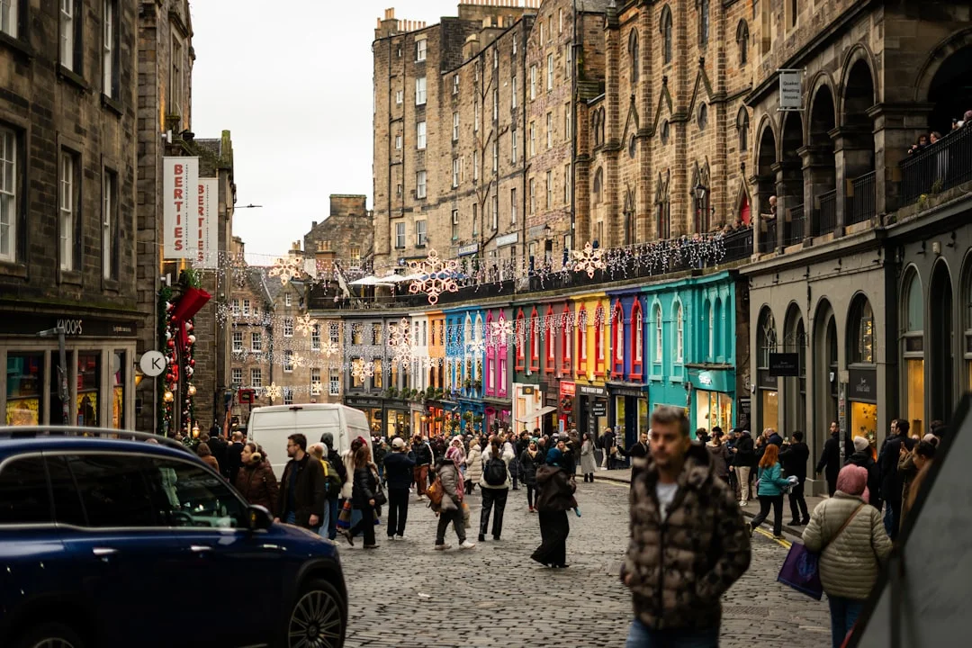 People walking on a cobblestone street lined with colorful shops and historic stone buildings in Edinburgh