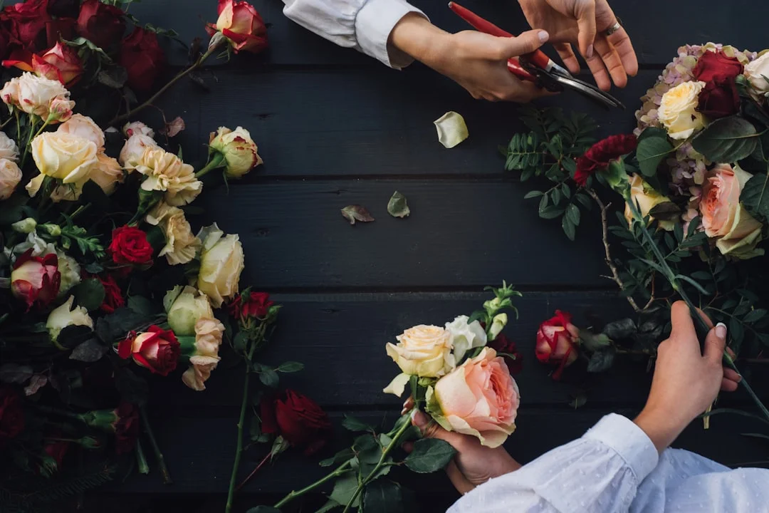 Hands cutting and arranging red and cream roses on a dark wooden table during a flower crown workshop