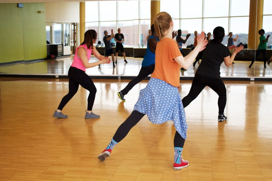 A group of women in athletic wear practicing a dance routine in a studio with large mirrors and wooden floors