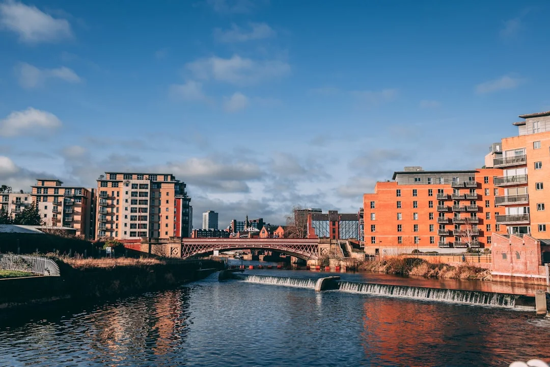 A river with a small weir flows through Leeds city centre, past modern apartment buildings and an arched bridge