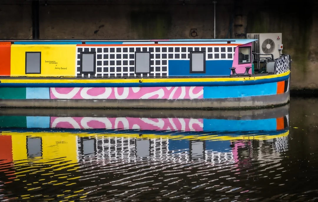 Colorful narrowboat with geometric patterns and pink abstract designs reflected in the Leeds canal water