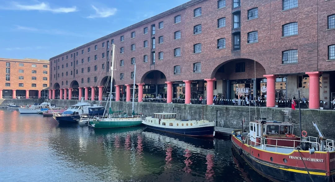 Brick buildings with pink columns and arched walkways overlook a dock with several moored boats in Liverpool