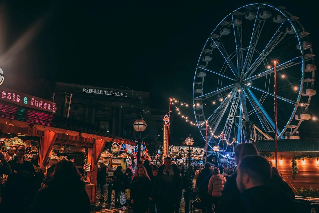 A crowded carnival at night with a large Ferris wheel and stalls near the Empire Theatre in Liverpool