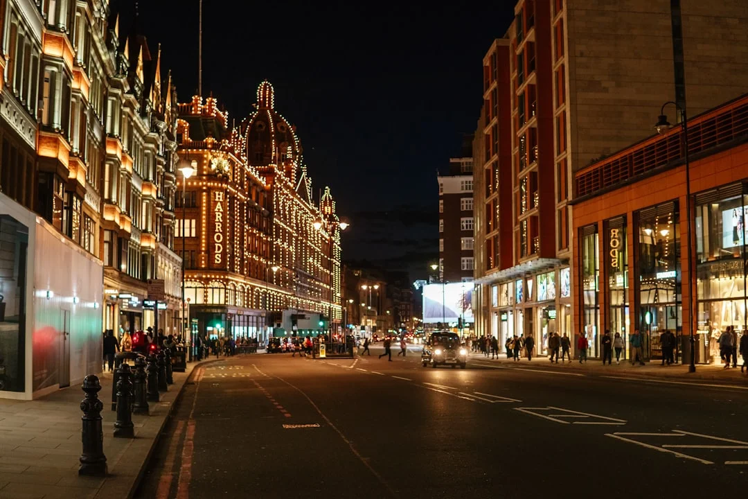 Harrods department store illuminated with golden lights at night on a London street with pedestrians and cars