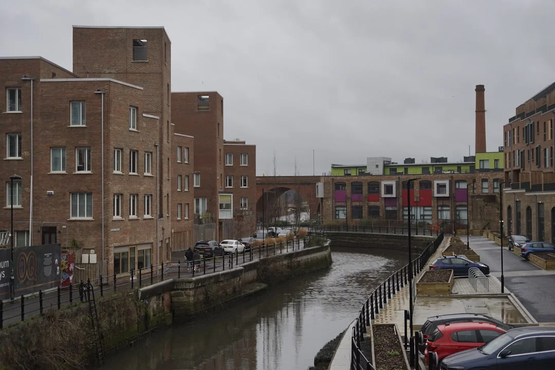 A river flows past brick buildings and under a stone arch bridge on a cloudy day in Newcastle
