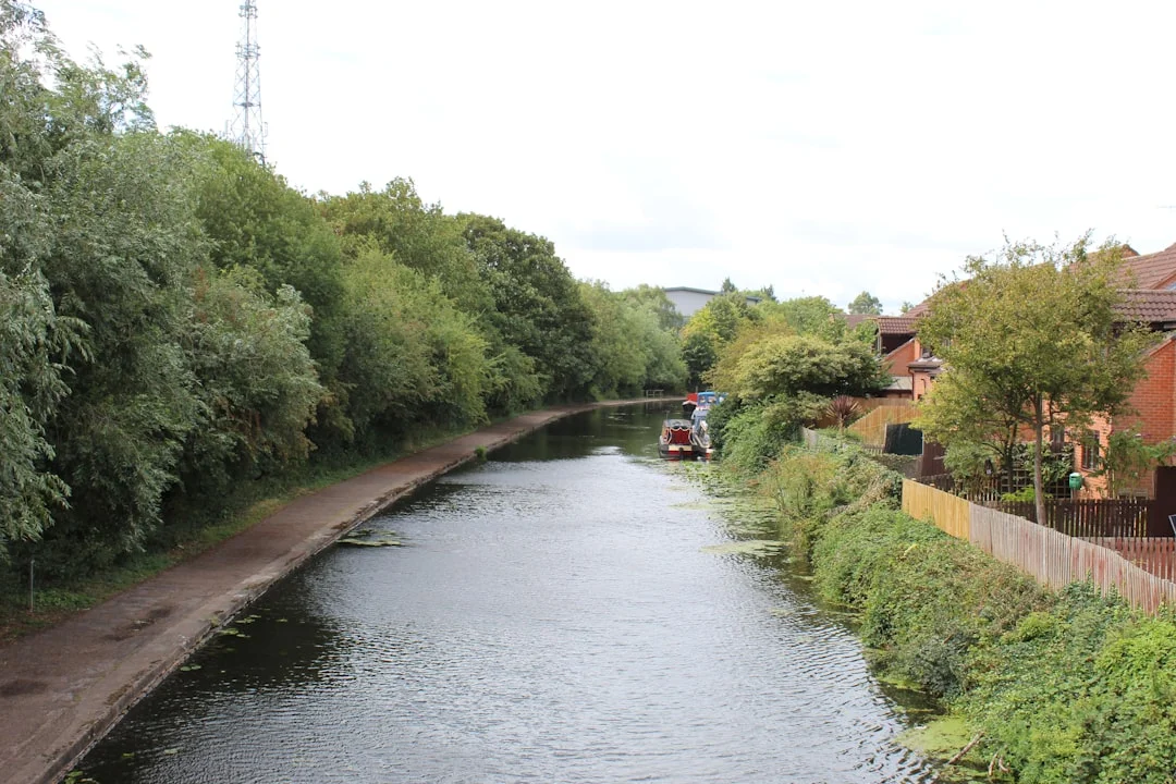 A canal flows through Nottingham, lined with lush green trees, a towpath, and residential houses