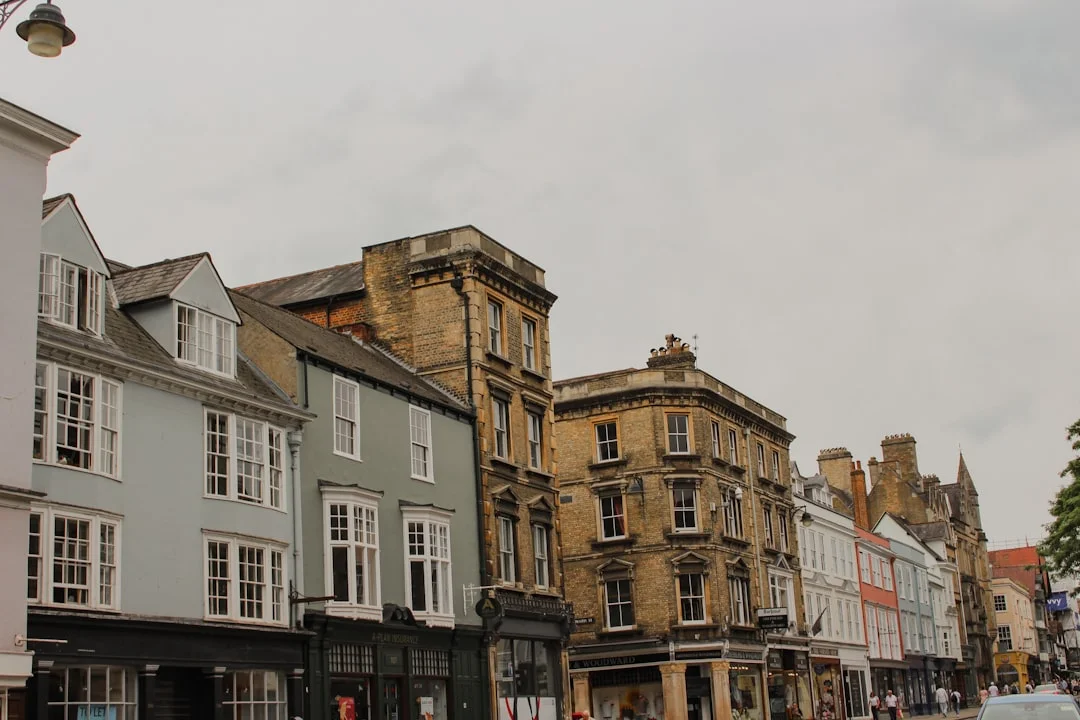 Row of historic multi-story buildings with shops on the ground floor under an overcast sky in Oxford