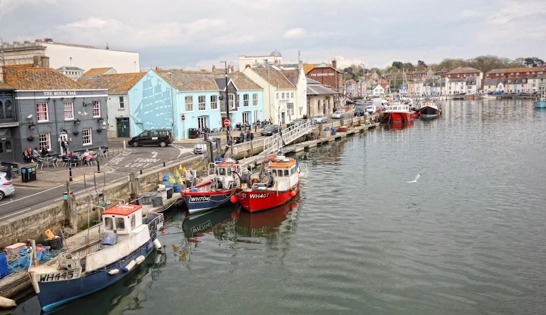Fishing boats moored in Weymouth Harbour with colorful buildings along the waterfront under a cloudy sky