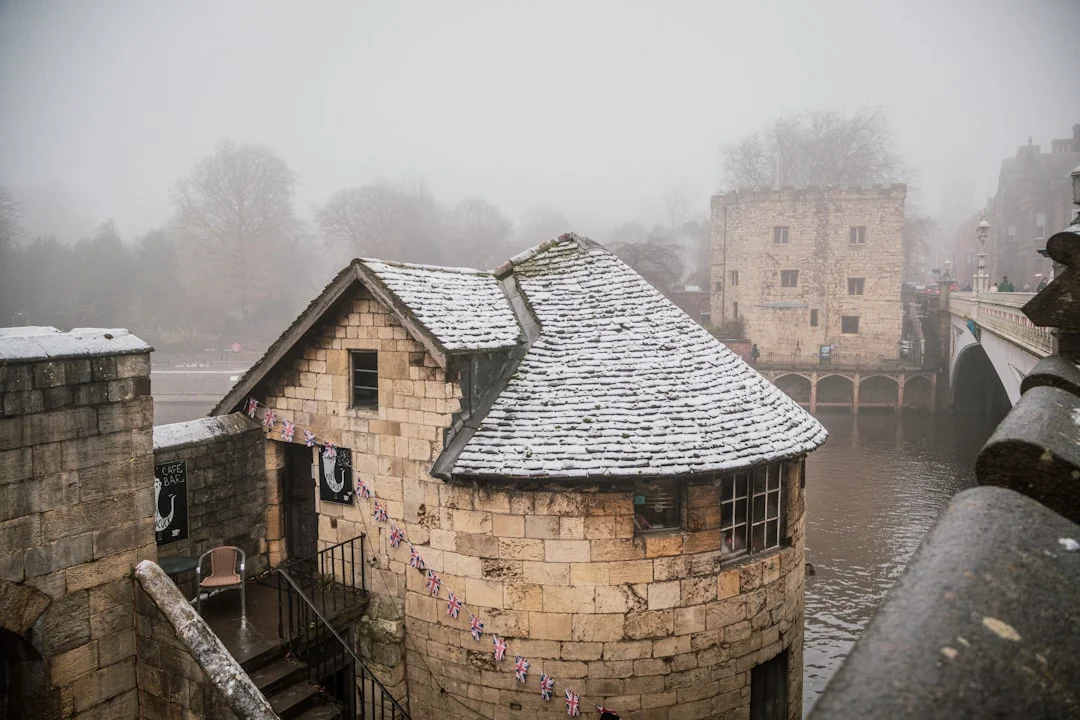 A stone building with a snow-dusted roof sits beside a river in York on a foggy winter day