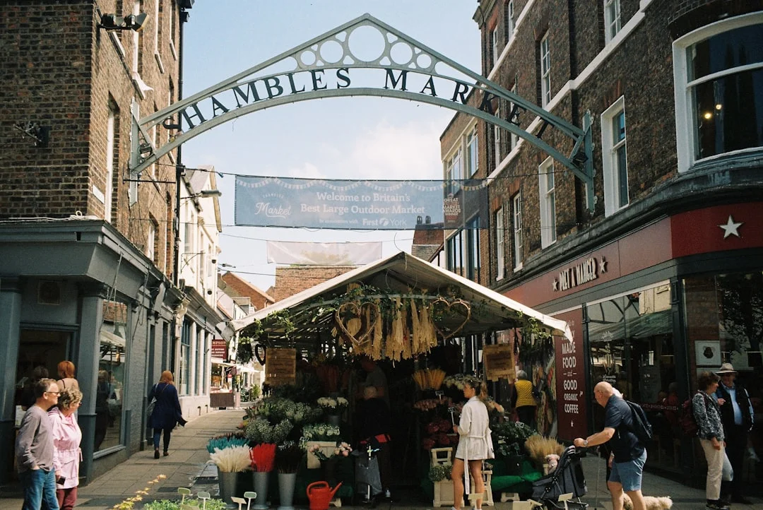 People walk past a flower stall under the Shambles Market archway in York