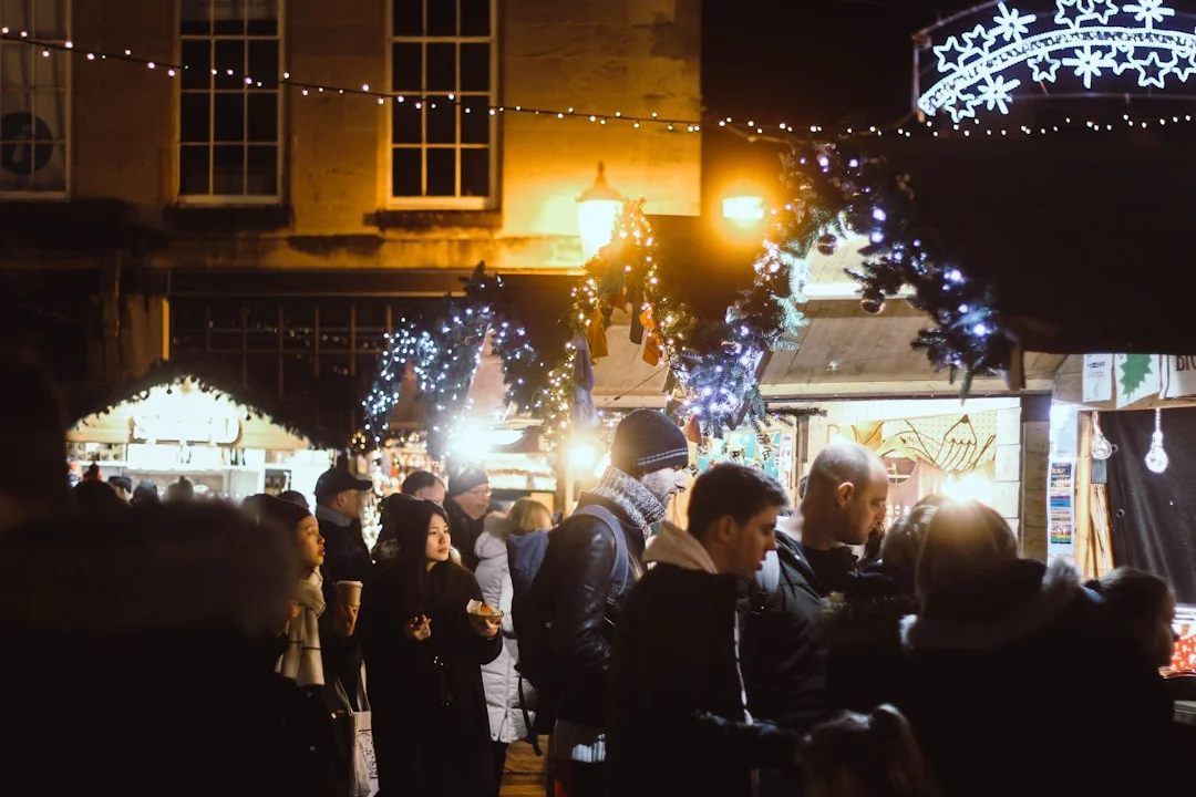 Crowds of people walk past festive wooden stalls and twinkling fairy lights at a night-time Christmas market