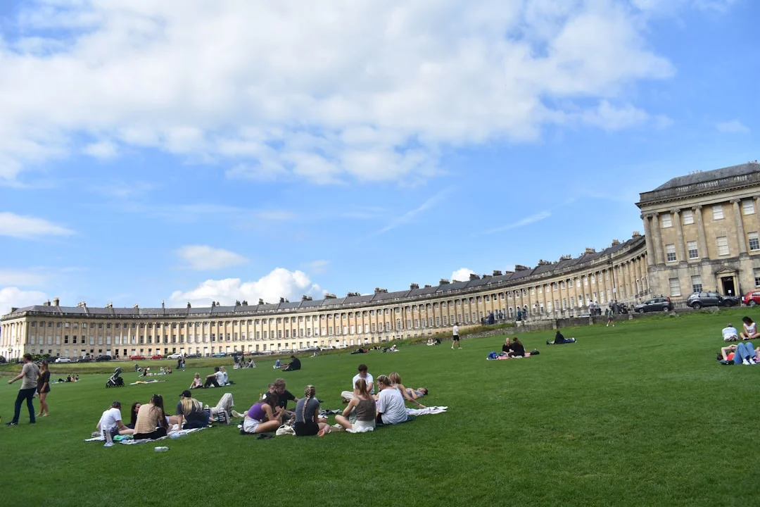 A long curved row of Georgian houses overlooking a green lawn with people picnicking in Bath, UK