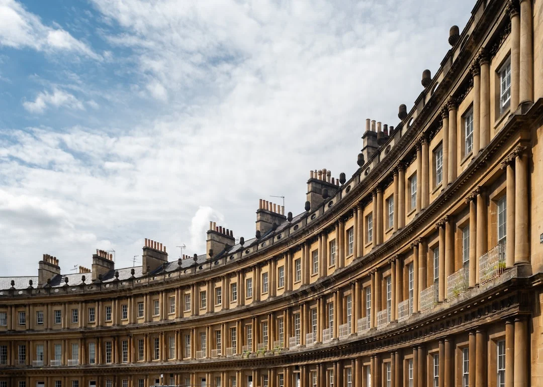 A curved Georgian building with multiple stories and columns under a blue sky in Bath