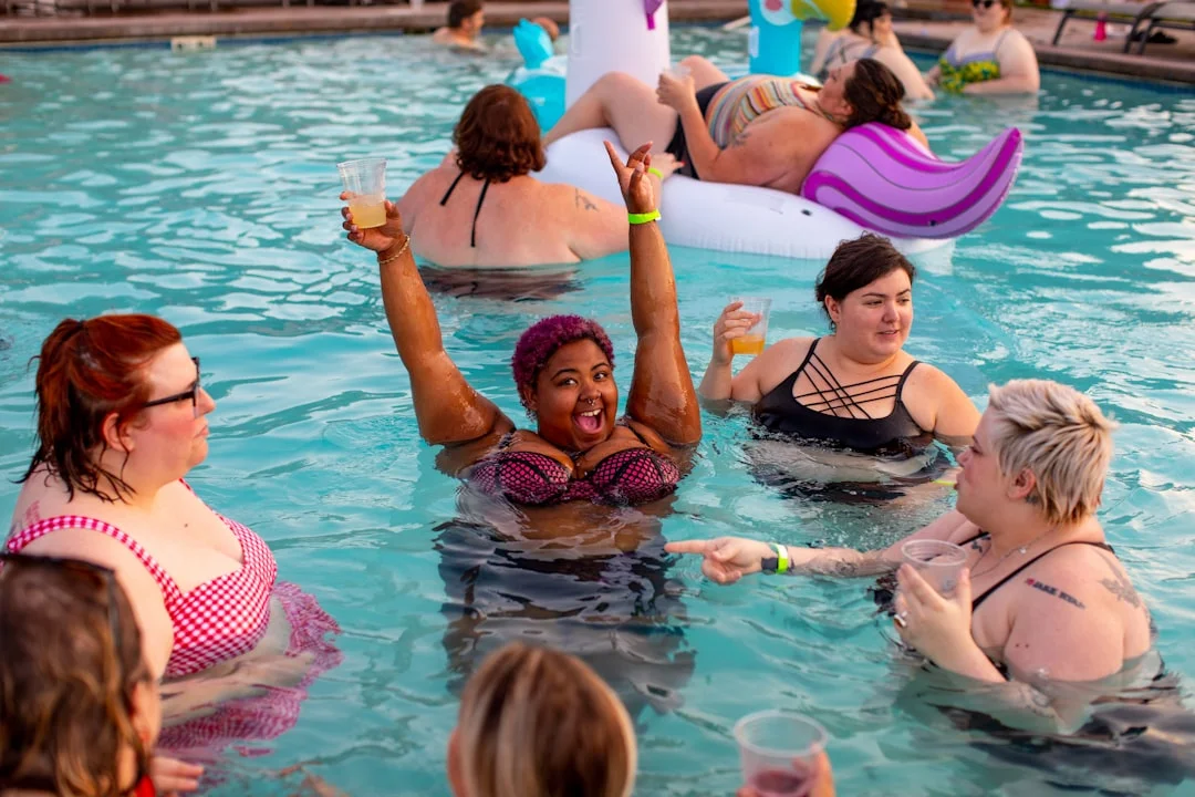 A group of women enjoy a pool party in Bath, with one woman cheering and raising her arms in the center