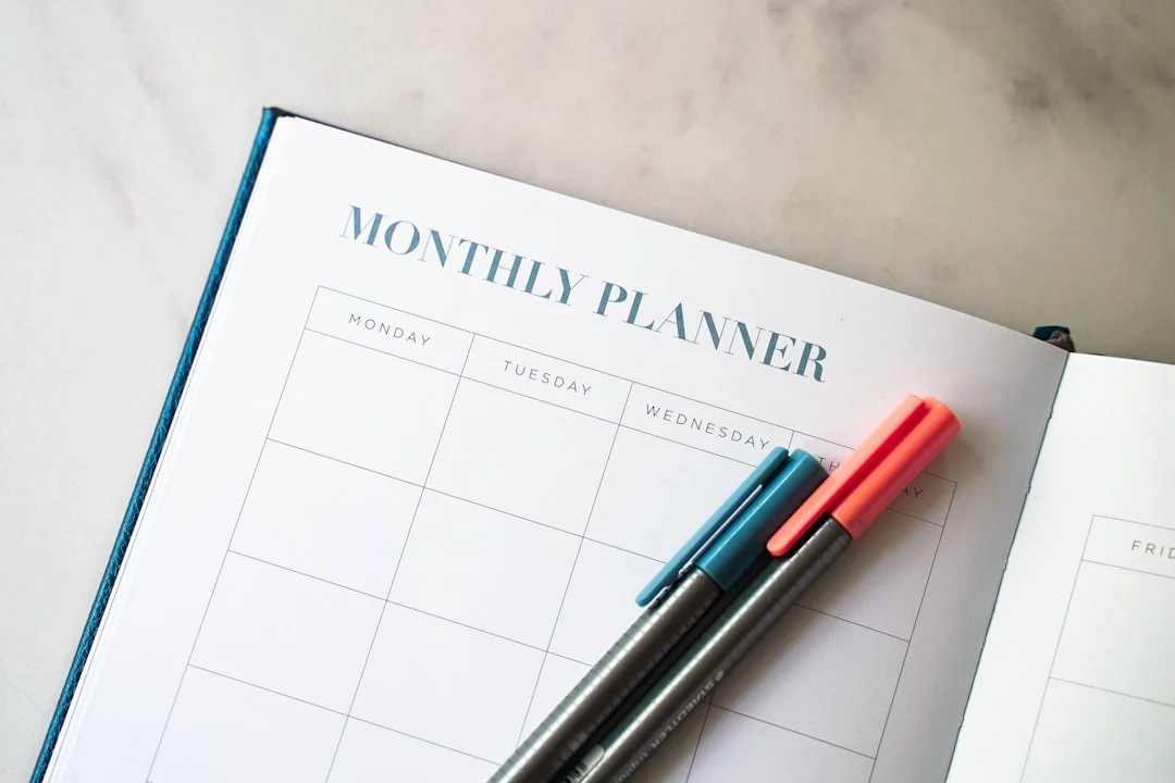 An open monthly planner with a grid layout and two pens resting on the page