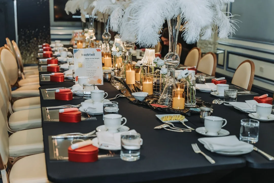 Elegant dining table with black cloth, white feather centerpieces, lit candles, and red heart-shaped gift boxes