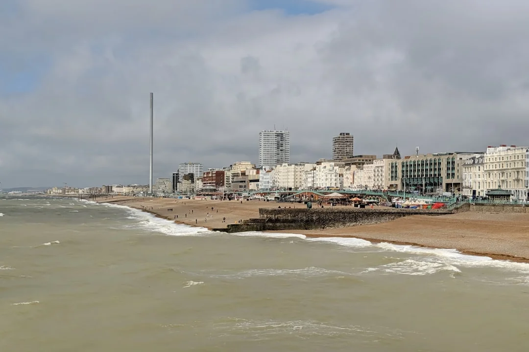 Brighton pebble beach and seafront buildings under a cloudy sky with the i360 tower in the distance