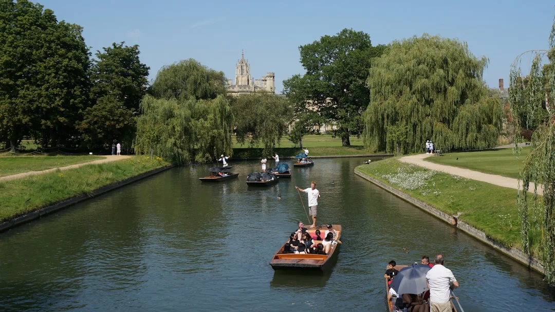 People punting on a river lined with willow trees and historic buildings in Cambridge