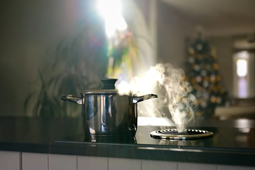 A stainless steel pot on a black stovetop with steam rising under bright sunlight