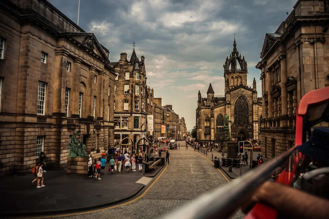 Cobbled street in Edinburgh with historic stone buildings and St Giles' Cathedral under a cloudy sky