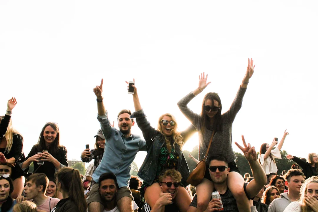 A crowd of young people cheering and sitting on shoulders at a sunny outdoor festival in Liverpool