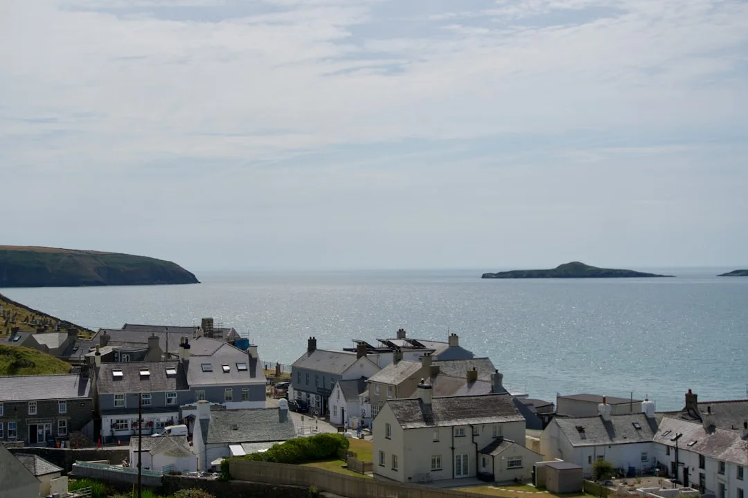 Traditional stone houses in a coastal village overlooking a calm sea with distant islands under a soft sky