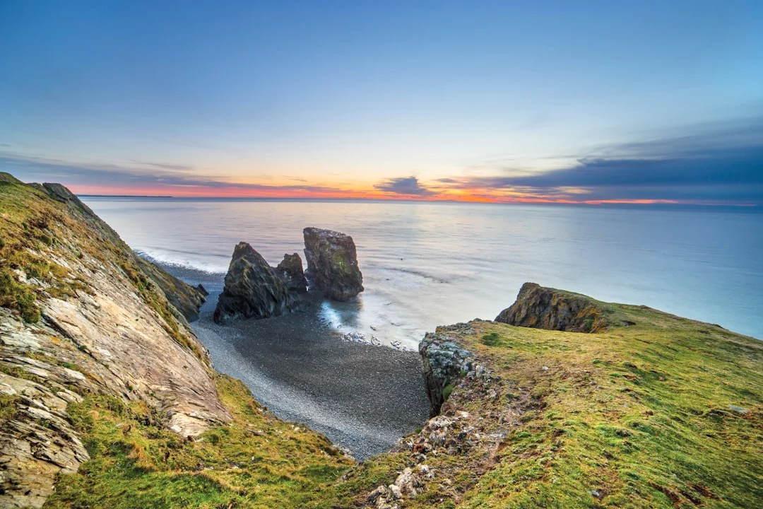 Sea stacks on a pebble beach below grassy cliffs at sunset on the Llŷn Peninsula