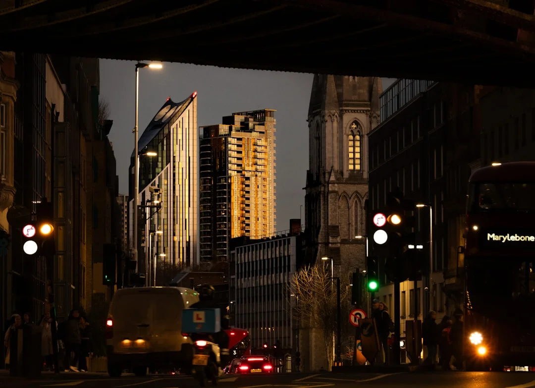 Sunset light glows on London skyscrapers and a church tower, framed by a bridge with evening traffic below