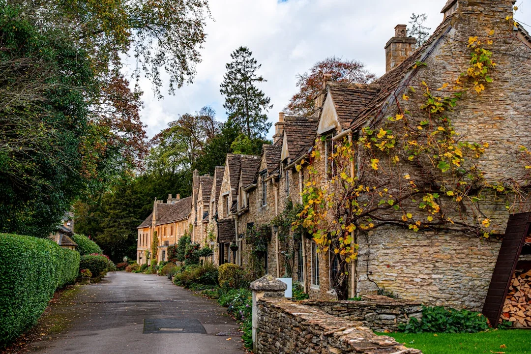 Honey-colored stone cottages line a quiet lane in Castle Combe, Cotswolds, framed by autumn foliage