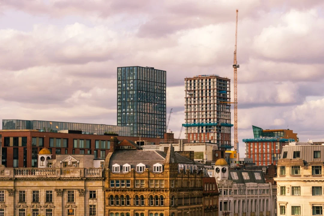 Manchester skyline featuring a mix of historic stone buildings and modern glass skyscrapers under a cloudy sky
