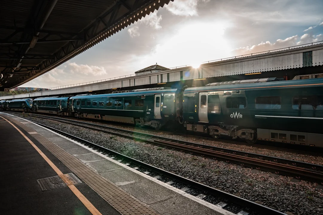A green Great Western Railway train at Brockenhurst station platform with the sun shining behind it