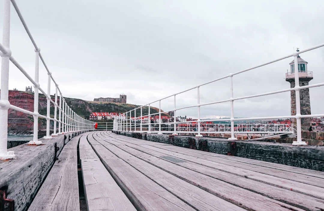 Wooden pier with white railings leading towards Whitby town and the Abbey on the cliffside