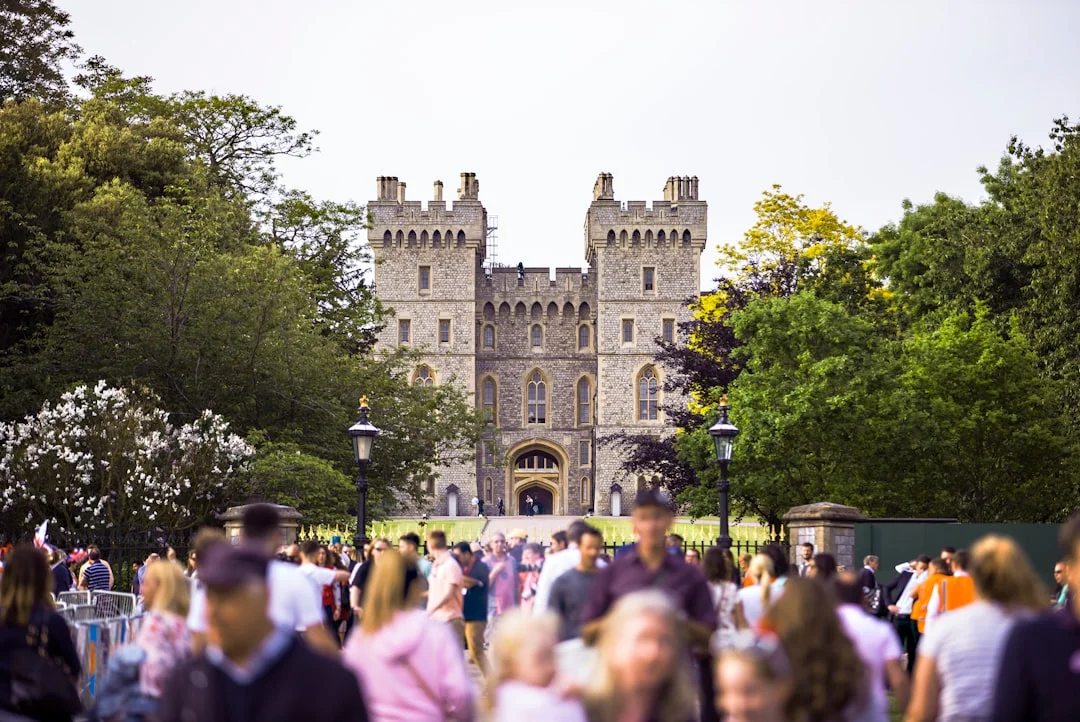 A large crowd of people gathers in front of the stone towers and arched entrance of Windsor Castle