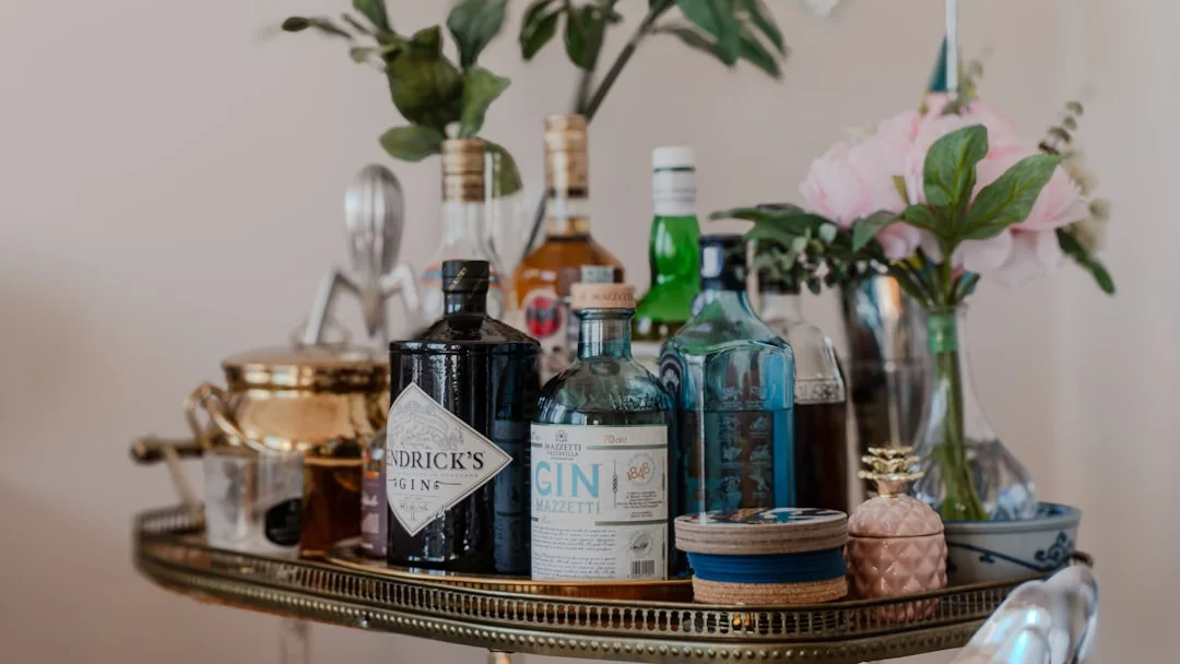A gold bar cart stocked with gin bottles, cocktail tools, and a vase of pink flowers
