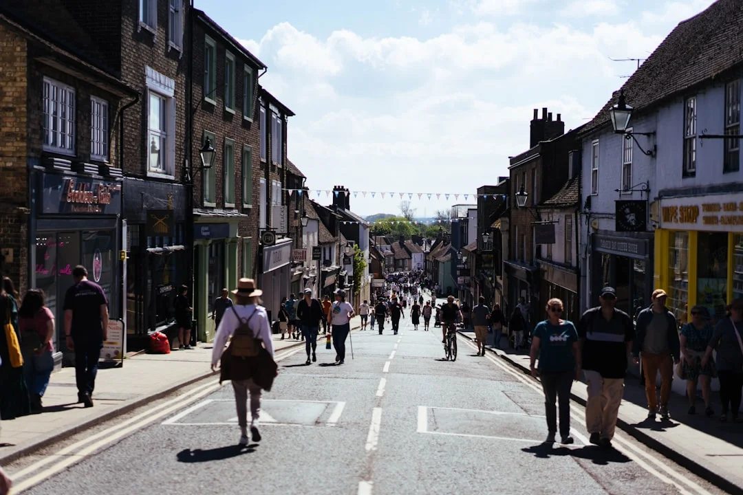People walk down a historic street lined with shops and brick buildings under a bright sky in Eton