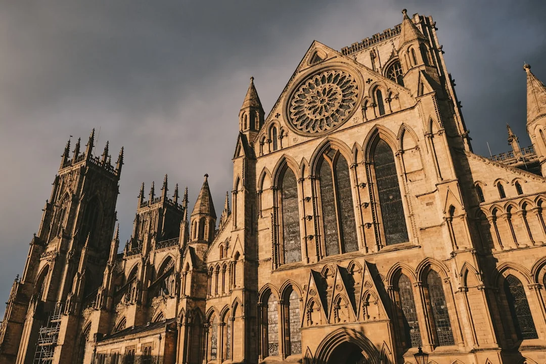 The grand Gothic facade of York Minster with its iconic rose window and towering stone spires under a moody sky