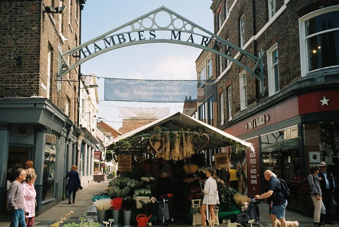 People walk past a flower stall under the Shambles Market archway in York