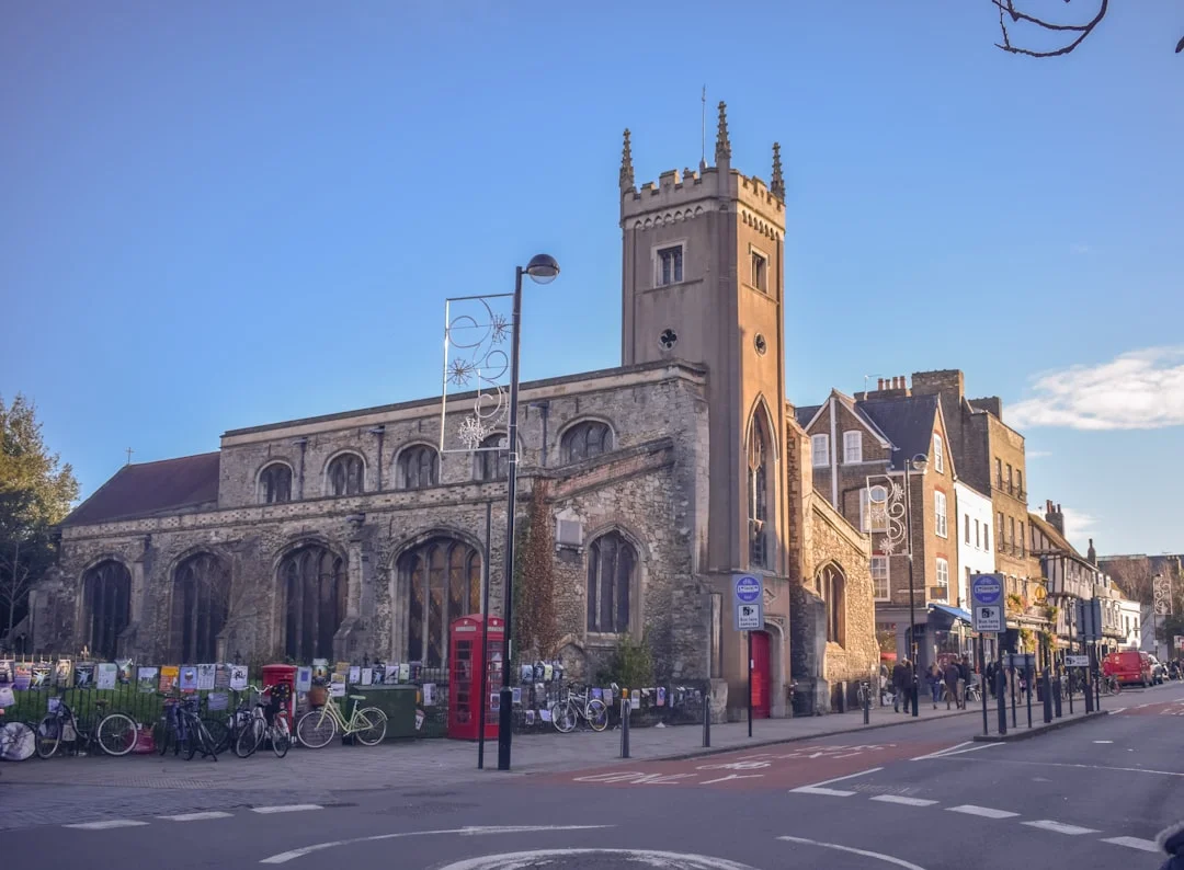 Historic Cambridge street with St Bene't's Church, parked bicycles, and a red telephone box on a sunny day