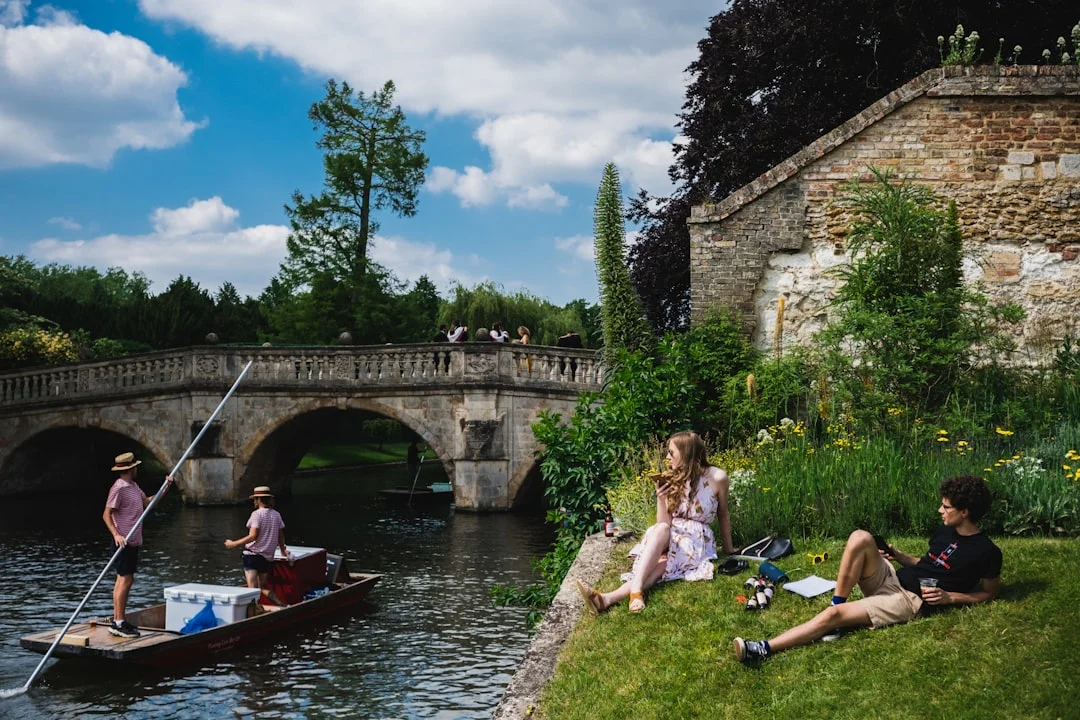 People punting on the River Cam in Cambridge, with others enjoying a picnic on the sunny riverbank