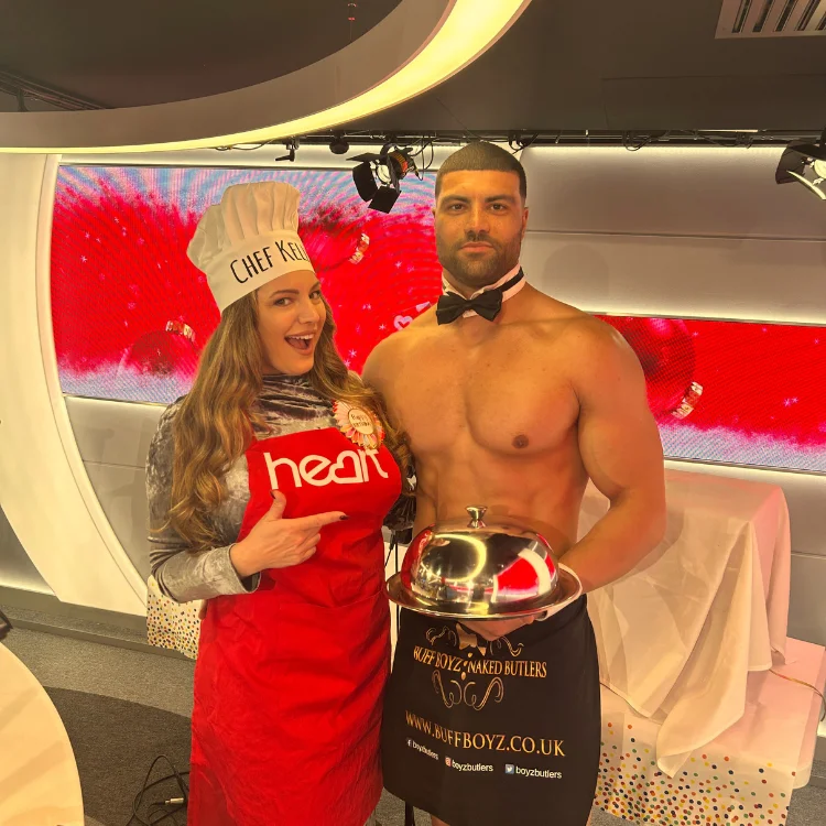 Two cheeky butlers in aprons serving drinks to a group of women at a hen party.
