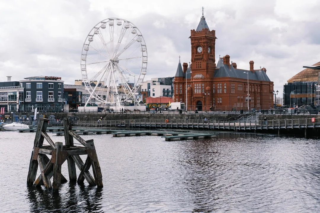 Cardiff Bay waterfront with a large Ferris wheel and the historic red brick Pierhead Building under a cloudy sky
