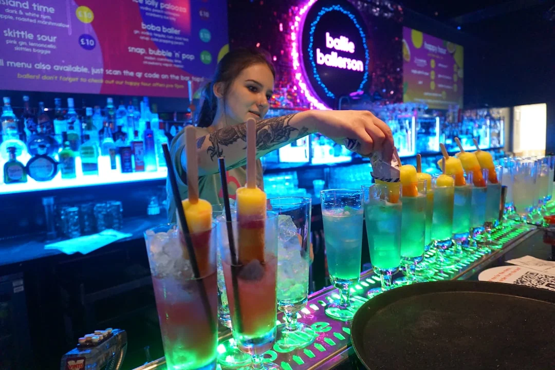 Bartender making colorful cocktails at a neon-lit bar on Caroline Street, Cardiff, showcasing nightlife