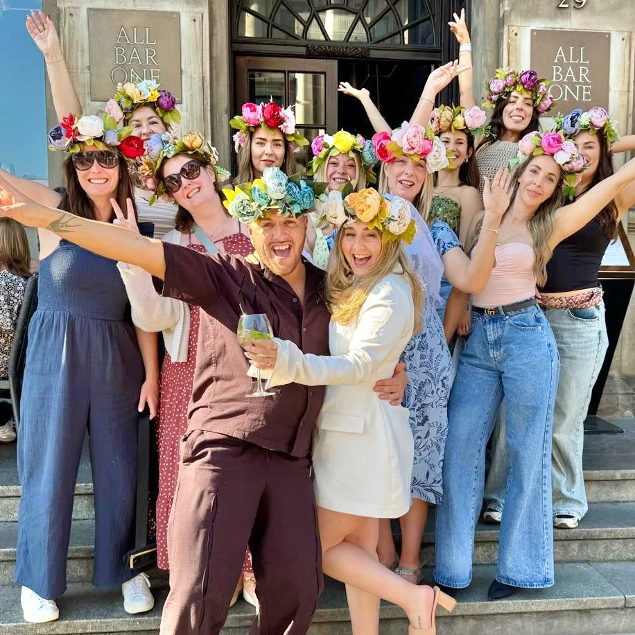 A hen party group smiling and holding up their creations at a flower crown making workshop.