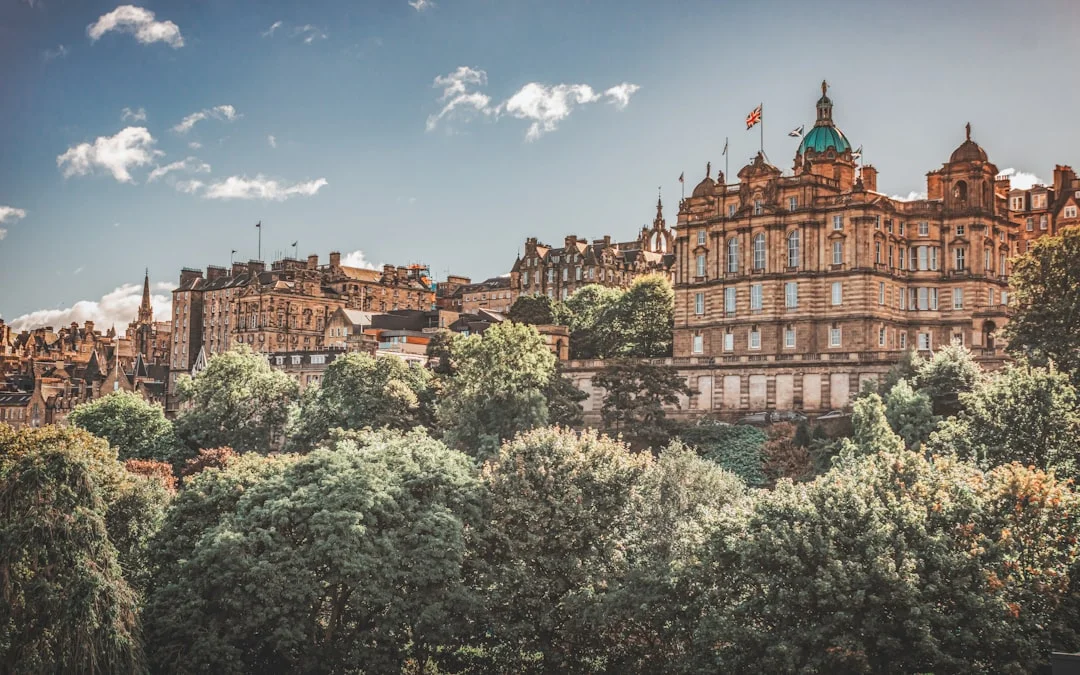 Edinburgh Old Town historic buildings nestled among vibrant green trees under a blue sky