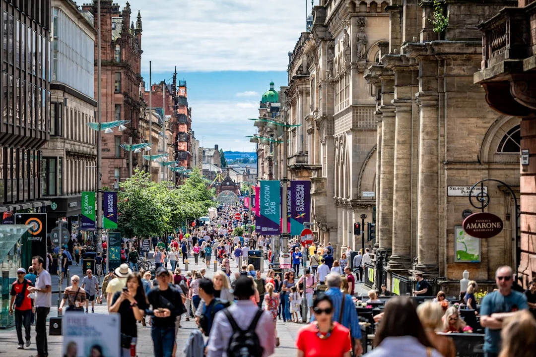 A busy Buchanan Street in Glasgow filled with people walking between historic buildings on a sunny day